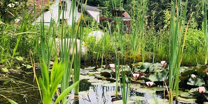 Naturhotel - Wasserbehandlung/ Energetisierung: Verwirbeltes Wasser - Gamlitz - Blick über den runden Teich zum Gebäude mit der Rezeption. - TamanGa Lebensgarten
