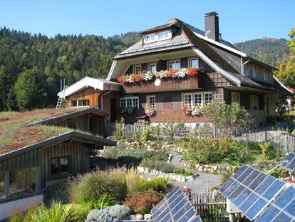 Naturhotel - Energieversorgung: Photovoltaik - Schwarzwald - Haus Sonne im Sommer, im Vordergrund der Kräutergarten und Solarpanels. - Haus Sonne - das vegetarische Bio-Hotel