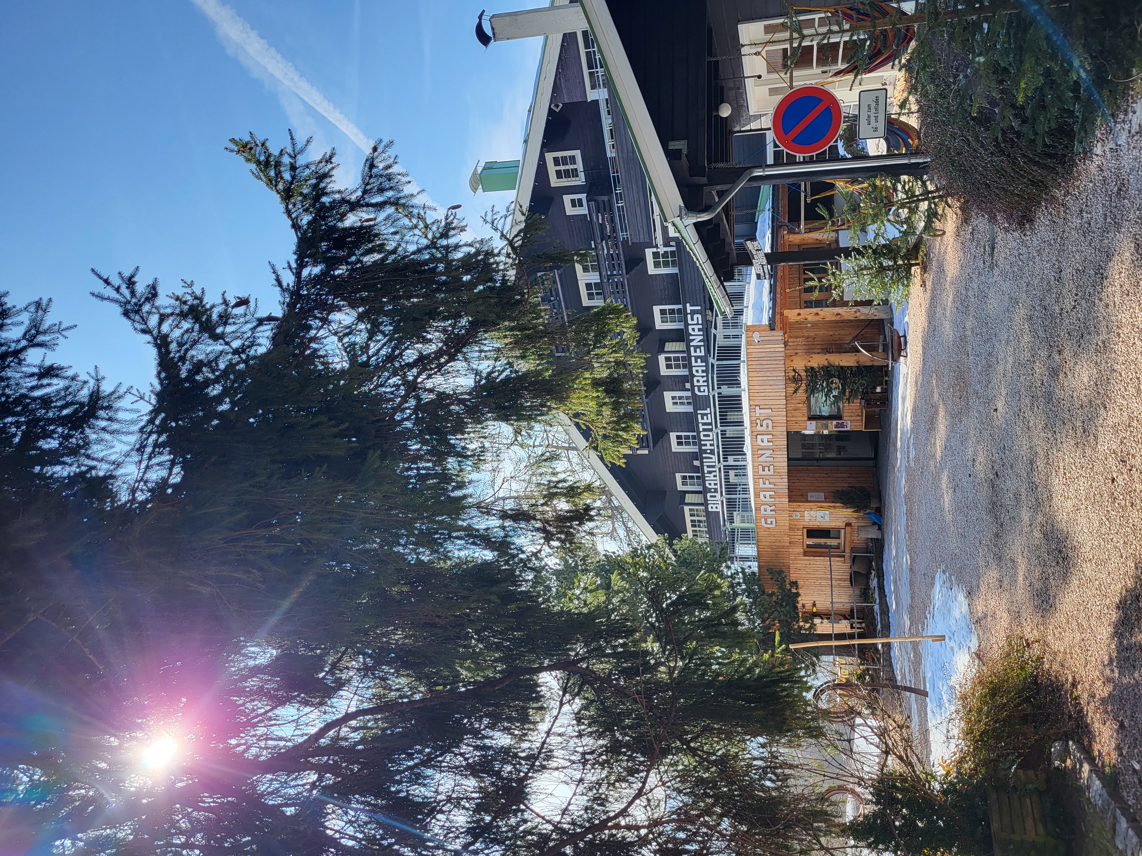 Organic hotel - Das Biohotel Grafenast begrüßt seine Gäste auf eine ganz besondere, unaufdringliche Weise – der Eingangsbereich verkörpert perfekt die Philosophie des Hauses: natürlich, künstlerisch, familiär und weit entfernt von sterilem Hotel-Luxus.
Beim Ankommen fällt sofort das traditionelle, dunkle Tiroler Holzhaus ins Auge, mit seinem markanten Satteldach, grünen Akzenten und der typischen, wettergegerbten Fassade, die sich harmonisch in die Berglandschaft einfügt. Der Eingang ist warm und einladend: Oft führt ein kleiner, überdachter Bereich oder eine Holztreppe direkt hinein, flankiert von natürlichen Elementen wie unbehandeltem Holz, Stein oder dezenten Kunstinstallationen. Im Inneren erwartet Sie eine Rezeption, die eher wie eine gemütliche Stube wirkt – mit viel Holz, offenen Regalen, vielleicht einer kleinen Theke und einer Atmosphäre, die sofort „Zuhause“ signalisiert. Gäste beschreiben den Bereich als modern-natürlich, mit hellen, allergikerfreundlichen Materialien, Kunstwerken der Familie und einem Hauch von Exzentrik, der das Grafenast so besonders macht. Kein übertriebener Prunk, stattdessen Authentizität: Hier spürt man sofort die tiefe Verbundenheit zur Natur und zur Kunst.

Die Geschichte des Biohotels reicht bis ins Jahr 1907 zurück – gegründet von Toni Unterlechner, liebevoll „Rodel-Toni“ genannt. Er errichtete damals nicht nur eine einfache Tiroler Pension, sondern baute auch den ersten Skilift in der Region und legte damit den Grundstein für den Tourismus am Pillberg. Aus dieser bescheidenen Anfangszeit entwickelte sich über vier Generationen hinweg ein echtes Pionierprojekt: In den 1980er Jahren wagte die Familie Unterlechner – damals schon als Rebellen gegen den Massentourismus – den radikalen Schritt hin zu Bio, Vollwertküche, Achtsamkeit und Nachhaltigkeit. 1986 nannte sich das Haus erstmals „Bio-Aktiv-Hotel Grafenast“ und gilt seither als eines der ersten Biohotels Tirols. Heute führt Peter Unterlechner zusammen mit seiner Frau Waltraud das Hotel in vierter Generation – klimaneutral, gemeinwohl-bilanzierend und mit viel Liebe zur Kunst, Musik und Natur. Was als einfache Bergpension begann, ist heute ein „Haus der begehbaren Erinnerung“: ein Ort, der Tradition bewahrt, Innovation lebt und Gäste einlädt, die Seele baumeln zu lassen.
Der Eingang ist somit nicht nur der Beginn eines Aufenthalts, sondern der Einstieg in über 115 Jahre gelebte Gastfreundschaft – authentisch, nachhaltig und voller Charakter. - Biohotel Grafenast