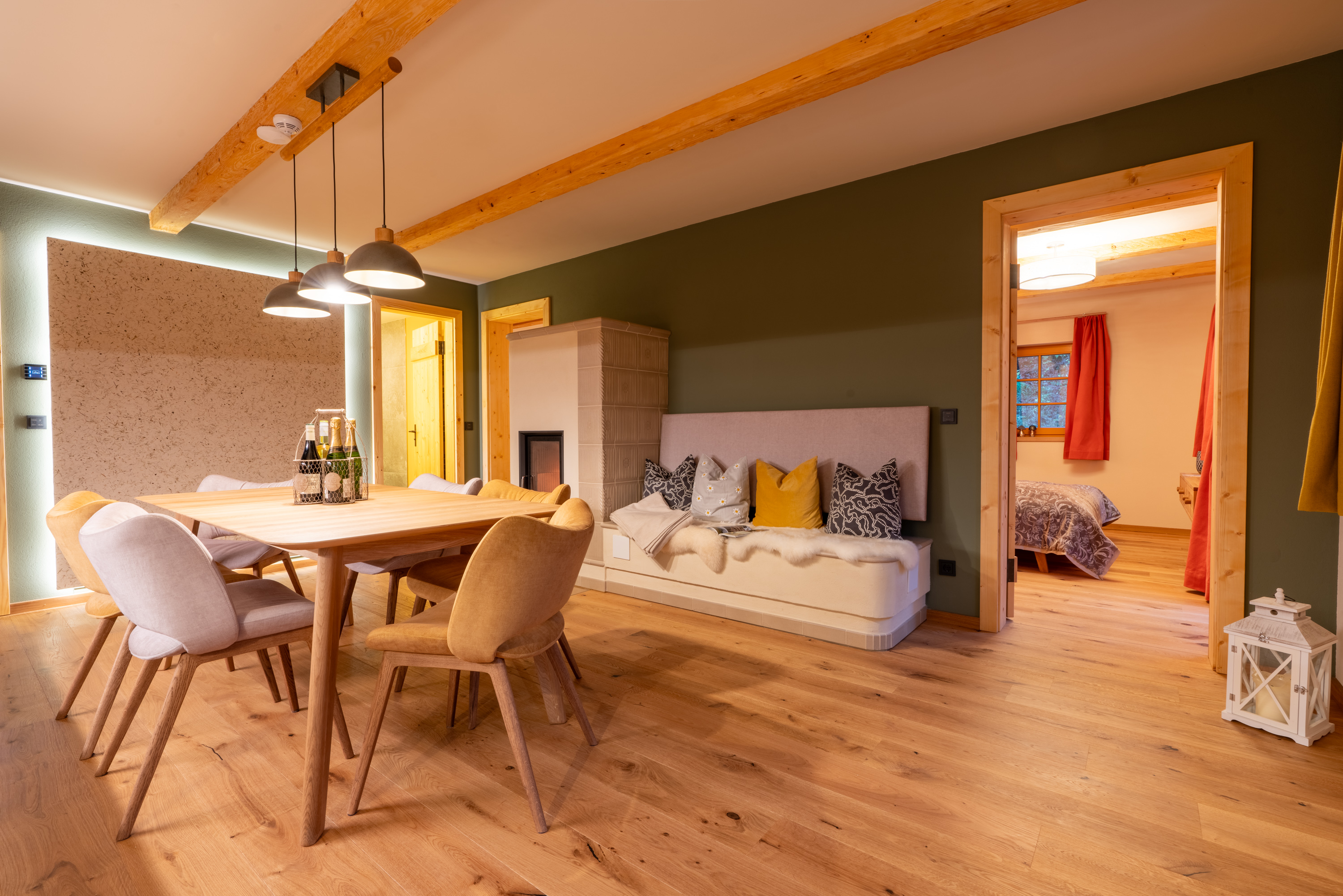 Biohotel: Unsere Ringelblume: Eindruck der Wohnküche mit gemütlichem Kachelofen. Rechts das Schlafzimmer mit eigenem Balkon. Links vom Kamin befindet sich der Zugang zum zweiten Schlafzimmer und dem Bad mit bodenebender, verglaster Dusche. - BIO-NATURIDYLL WIESENGRUND