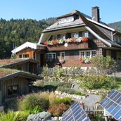 Naturhotel: Haus Sonne im Sommer, im Vordergrund der Kräutergarten und Solarpanels. - Haus Sonne - das vegetarische Bio-Hotel